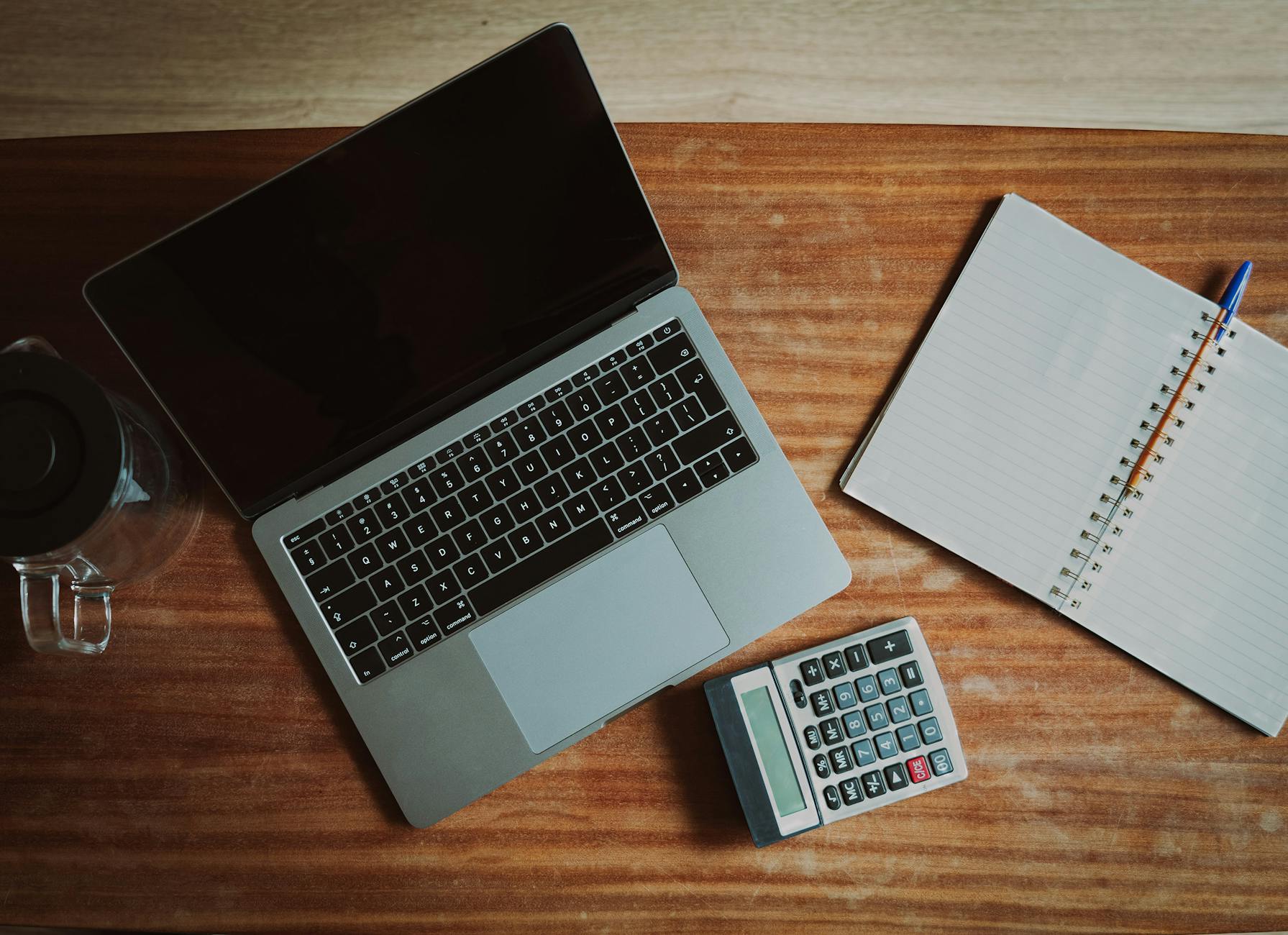 Aufsicht auf einen Schreibtisch mit Laptop und Taschenrechner